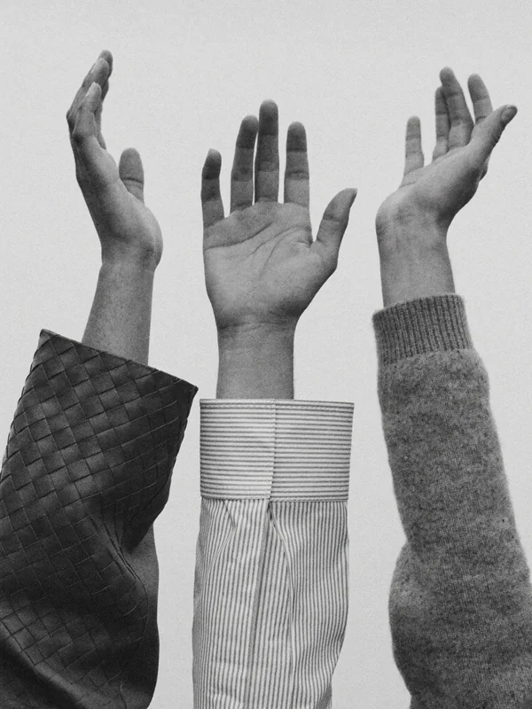 Three raised forearms in different fabrics — woven leather, a striped shirt cuff and a wool knit — against a pale sky.